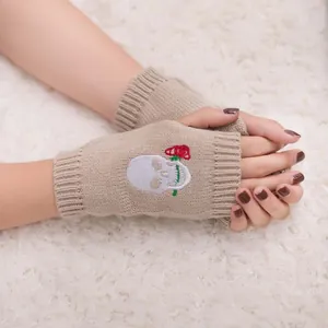 Dettaglio del ricamo teschio e rosa sui guanti senza dita in maglia beige