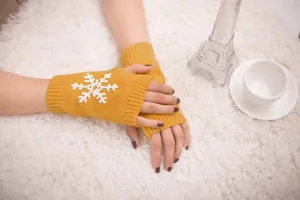 Detailed view of yellow knitted fingerless gloves with white snowflake embroidery