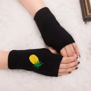 Vue détaillée de la broderie ananas jaune sur des mitaines tricotées noires.