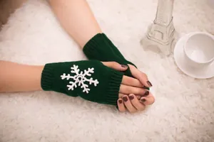 Close-up of dark green knitted fingerless gloves with white snowflake embroidery