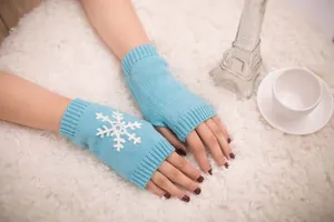 Blue knitted fingerless gloves with white snowflake motif worn in cozy winter setting.