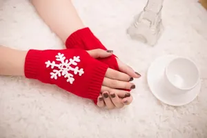 Detail of red knitted fingerless gloves featuring a white snowflake embroidery design.