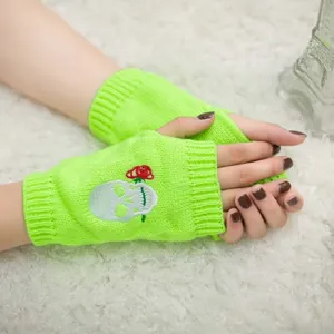 Dettaglio guanti senza dita verde neon con ricamo teschio e rosa su sfondo soffice