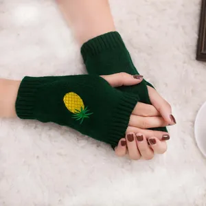 Gros plan de gants tricotés sans doigts vert foncé avec broderie d'ananas jaune.