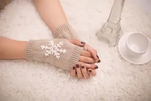 Detailed macro view of beige knitted fingerless gloves featuring a white snowflake patch.