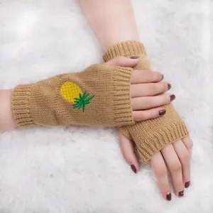 Gros plan de gants tricotés sans doigts avec broderie ananas sur fond blanc moelleux.