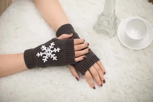 Close-up detail of white snowflake embroidery on warm dark gray knitted fingerless gloves
