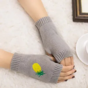 Gros plan de mitaines en tricot gris avec détails de broderie d'ananas jaune.