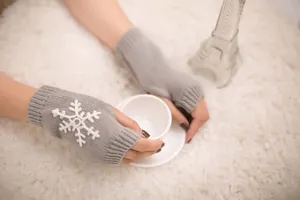 Detail view of grey knitted fingerless gloves with elegant white snowflake embroidery