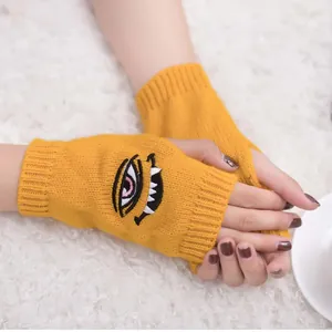 Nahaufnahme gelber Strickstulpen ohne Finger mit Dämonenauge- und Zahn-Stickerei.