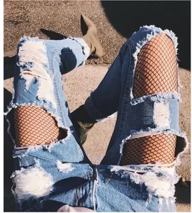 Macro detail view of sexy black fishnet tights worn under distressed denim jeans.