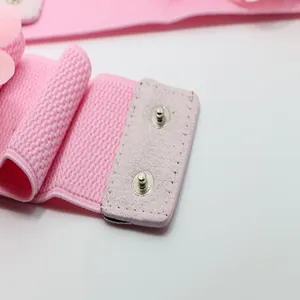 Close-up of pink elastic belt showing metal snap button closure and floral detail.