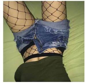 Close-up of black large-mesh fishnet stockings worn under denim shorts on green background