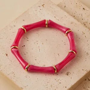 Vista de detalle de una pulsera de acrílico rosa con segmentos de bambú y anillos dorados