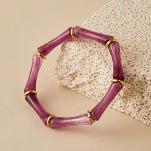 Primer plano de pulsera de acrílico púrpura con anillos dorados sobre piedra coral.
