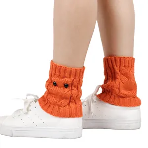 Close-up detail of orange owl-themed knitted leg warmers worn with white sneakers