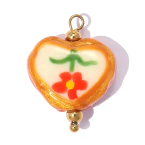 Détail d'un pendentif en céramique en forme de cœur avec fleur rouge et paillettes.