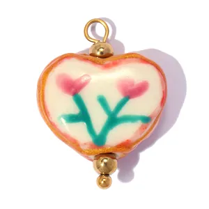 Gros plan d'un pendentif coeur en céramique fait main avec motif floral rose et doré