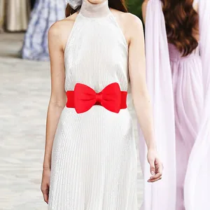 Close-up view of a vibrant red oversized bow elastic waist belt on a white pleated maxi dress