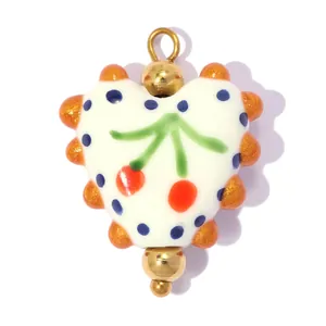 Vue macro détaillée d'un pendentif cœur en céramique avec motifs cerises et pois bleus.