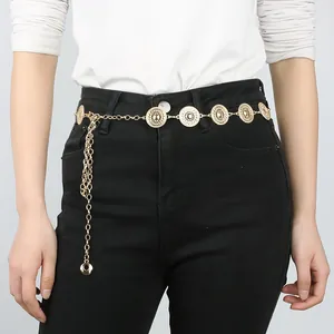 Dettaglio di cintura a catena dorata con dischi solari su jeans neri a vita alta