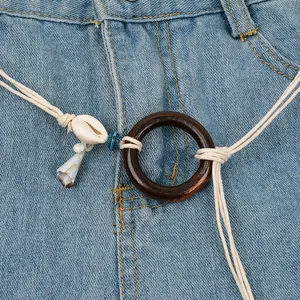Detailed view of a bohemian braided waist chain with a wood ring and shell on blue jeans
