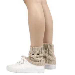 Close-up showing the intricate texture of beige knitted owl leg warmers on ankles