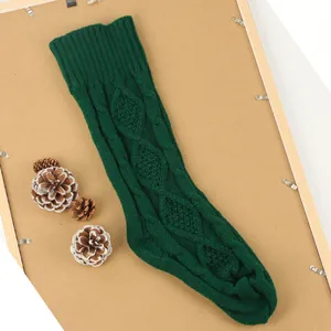 Détail d'une grande chaussette de Noël en tricot vert foncé sur un support en bois