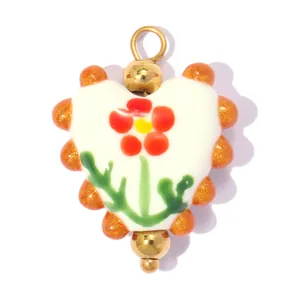 Gros plan d'un pendentif cœur en céramique avec motif floral rouge et détails dorés