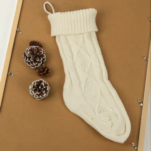 Gros plan d'une chaussette de Noël en tricot blanc avec des pommes de pin sur bois.
