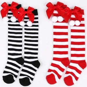 Detail view of striped kids knee-high socks with red bow and white pom-pom accents.