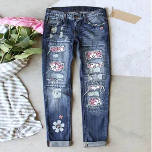 Detailed view of women's distressed denim jeans with floral print patches and embroidery.