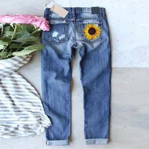 Close-up of women's slim-fit blue jeans featuring a back pocket sunflower print.