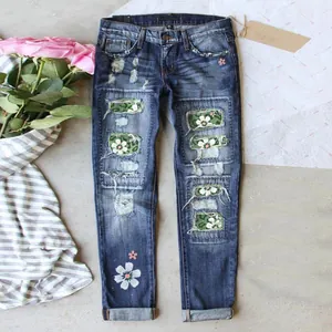 Distressed blue denim jeans for women featuring unique floral and camouflage patches.