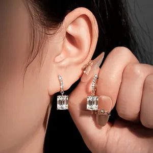 Close-up detail of elegant moissanite hoop earrings with emerald-cut stones on a model's ear.