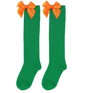Close-up detail of children's green knee-high socks featuring vibrant orange satin bows.