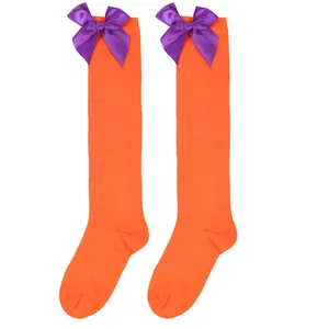 Detail of orange over-the-knee socks for girls featuring decorative purple bows