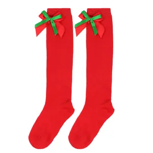 Detail of children's red Christmas over-the-knee socks with festive green ribbon bows