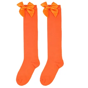 Detail of bright orange girls' knee-high socks featuring a large decorative satin bow.