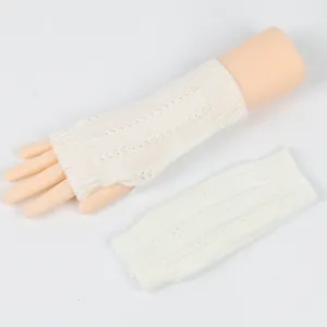 Weiße, zopfgestrickte, fingerlose Armstulpen auf einer Schaufensterpuppe und flach liegend.