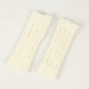 Detail of off-white cable-knit fingerless gloves showing intricate texture and warm material.