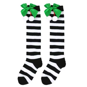 Close-up detail of festive girls' knee-high socks with black stripes and green bows.