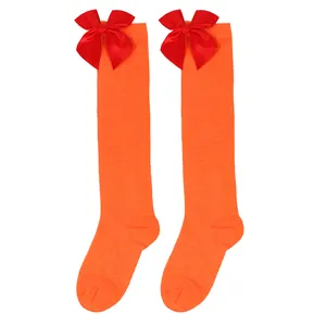 Close-up detail of vibrant orange girls' knee-high socks with festive red satin bows