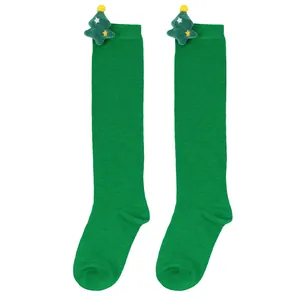 Close-up of green children's knee-high socks with cute plush Christmas tree ornaments.