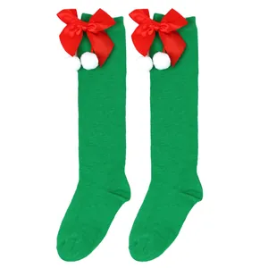 Detail view of festive green Christmas knee-high socks with red bow and white pom-poms