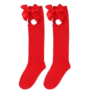Detailed view of red children's Christmas knee-high socks with bows and pom-poms
