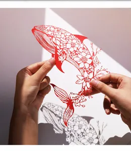 Vue détaillée d'un art du papier découpé de baleine rouge tenu sous la lumière naturelle.