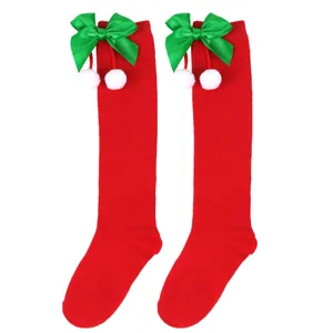 Detailed view of red children's Christmas knee-high socks with green bows and white pom-poms