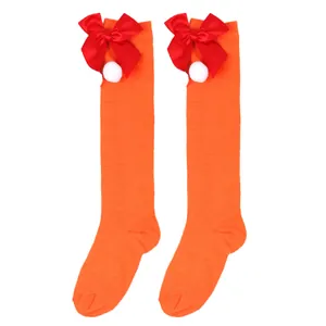 Close-up detail of orange knee-high Christmas socks featuring red bows and white pom poms