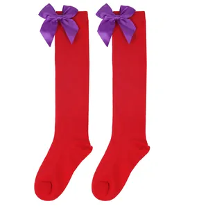 Detail of red children's knee-high socks featuring vibrant purple satin bows at the cuffs.